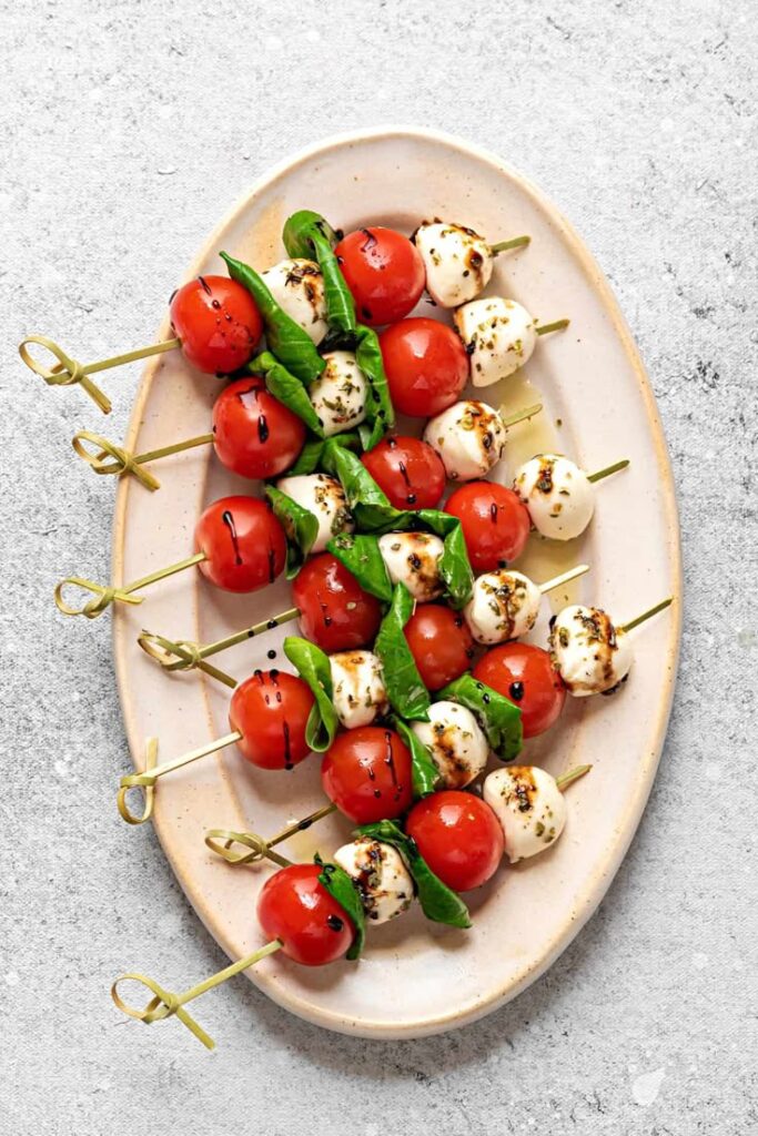 Caprese skewers with cherry tomatoes, mozzarella, and fresh basil on a plate. Perfect appetizer for parties.