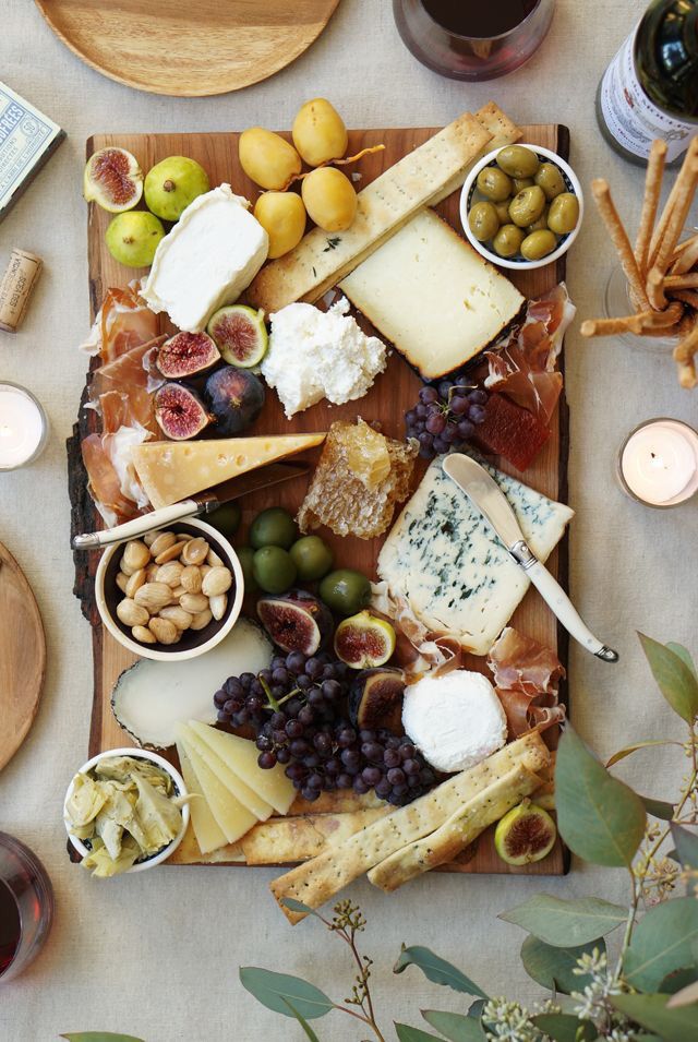 Assorted cheese board with figs, olives, nuts, and grapes on a wooden platter. Elegant gourmet appetizer display.
