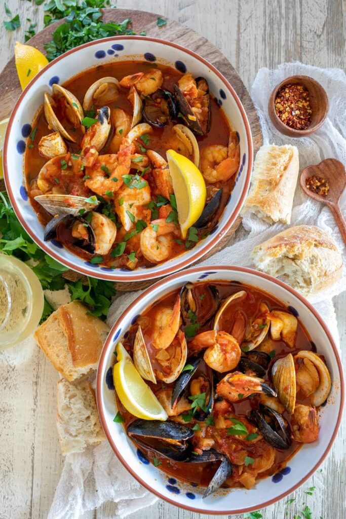 Hearty seafood stew with shrimp, mussels, and clams in tomato broth, garnished with lemon wedges and fresh parsley.