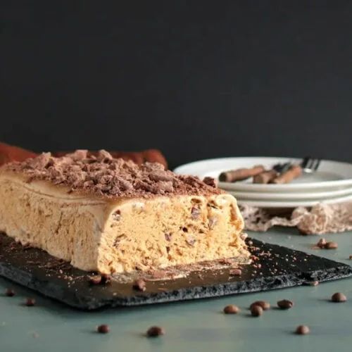 Delicious coffee ice cream cake topped with chocolate shavings on a dark slate platter, perfect dessert treat.