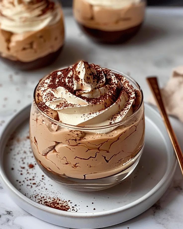 Creamy tiramisu dessert in glass with cocoa topping, served on a white plate, perfect for chocolate lovers.