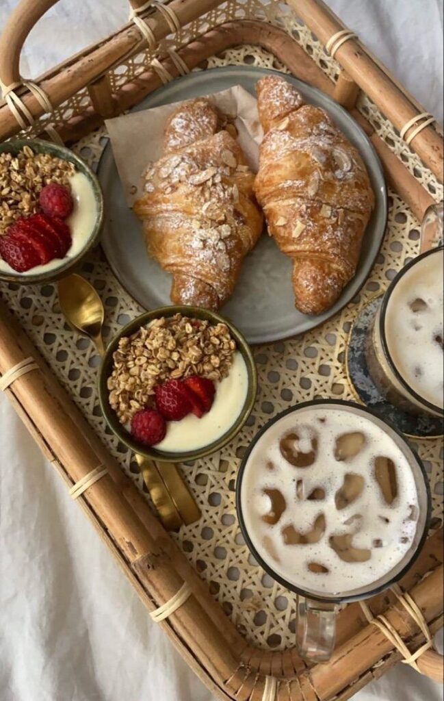 Breakfast tray with croissants, yogurt parfaits, and iced coffee on a wicker tray.
