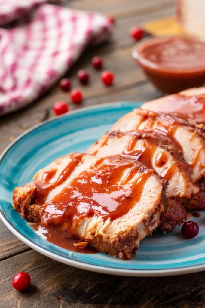 Sliced turkey breast with cranberry sauce on a blue plate, festive table setting with red berries.