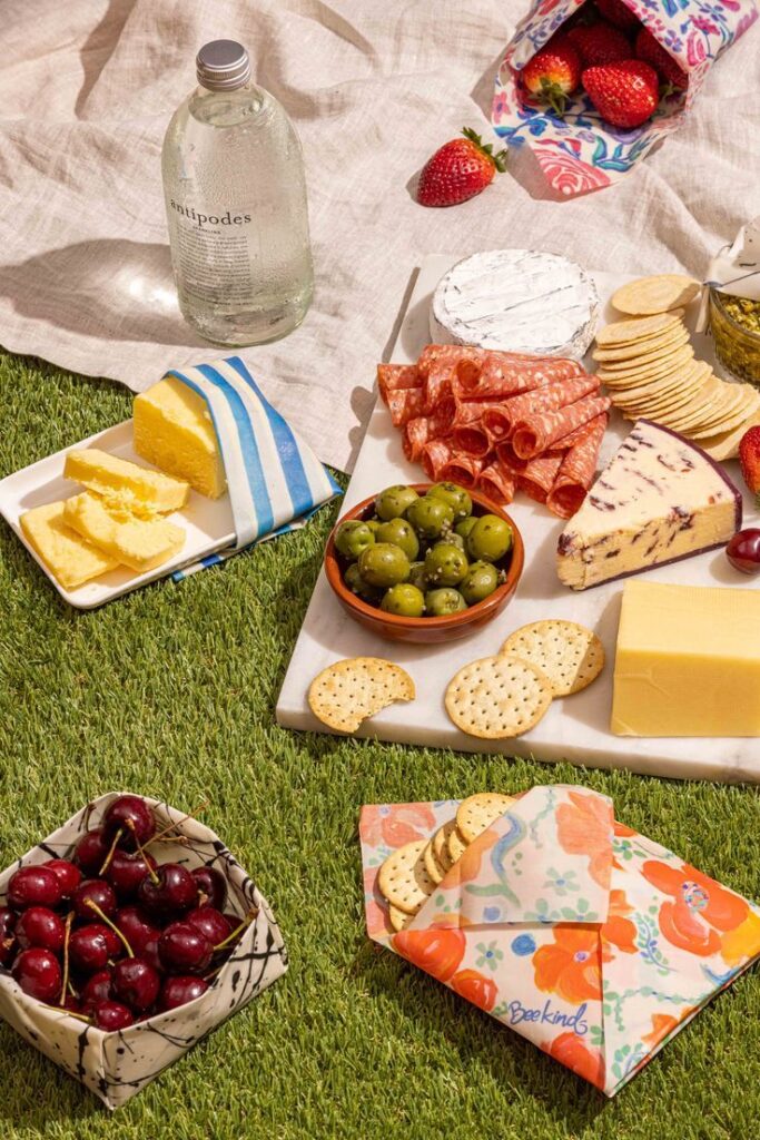 Picnic spread with cheeses, meats, olives, crackers, cherries, and bottled water on grass. Summer outdoor dining.
