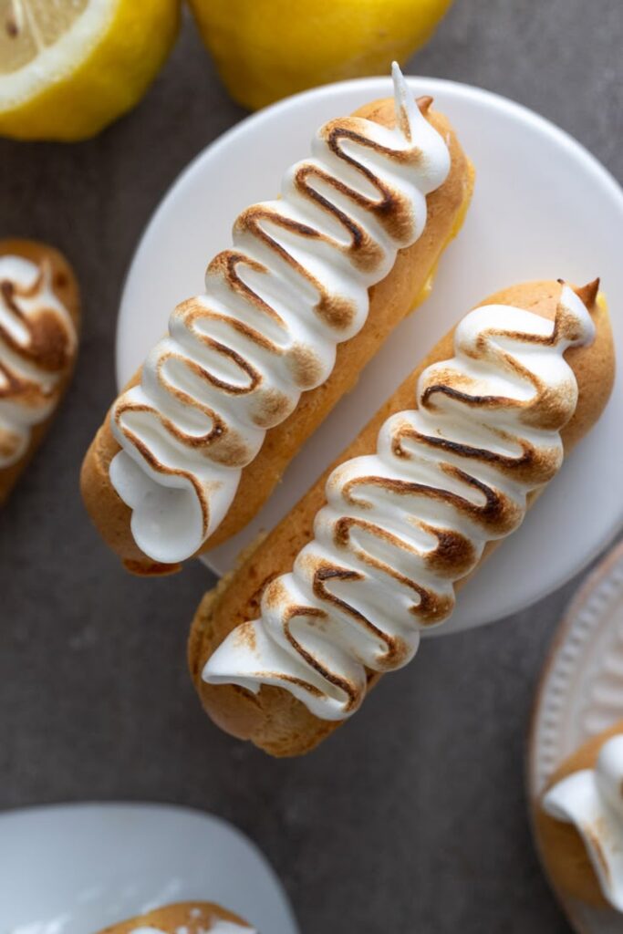 Golden éclairs with toasted meringue topping on a plate, surrounded by fresh lemons.