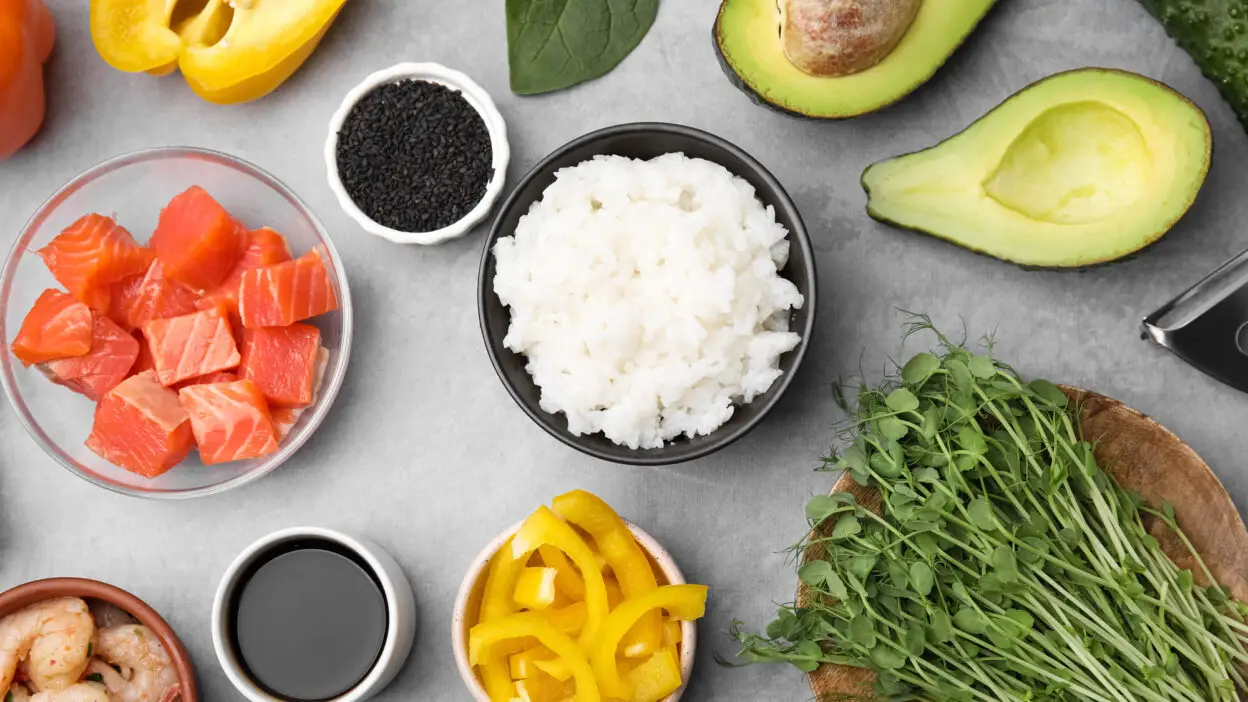 Sushi ingredients on a table: rice, salmon, avocado, shrimp, soy sauce, and vegetables. Fresh and colorful arrangement.