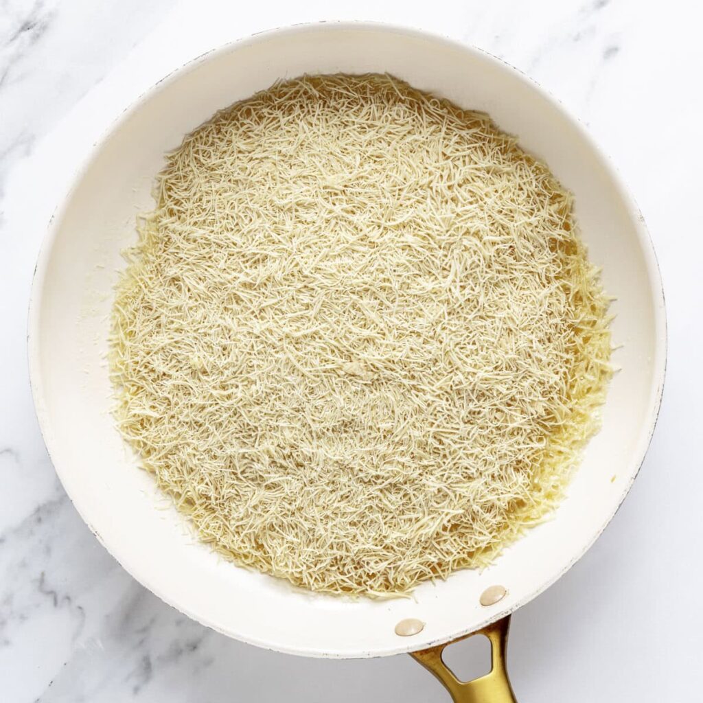 White pan with raw shredded phyllo dough on a marble surface, ready for cooking.