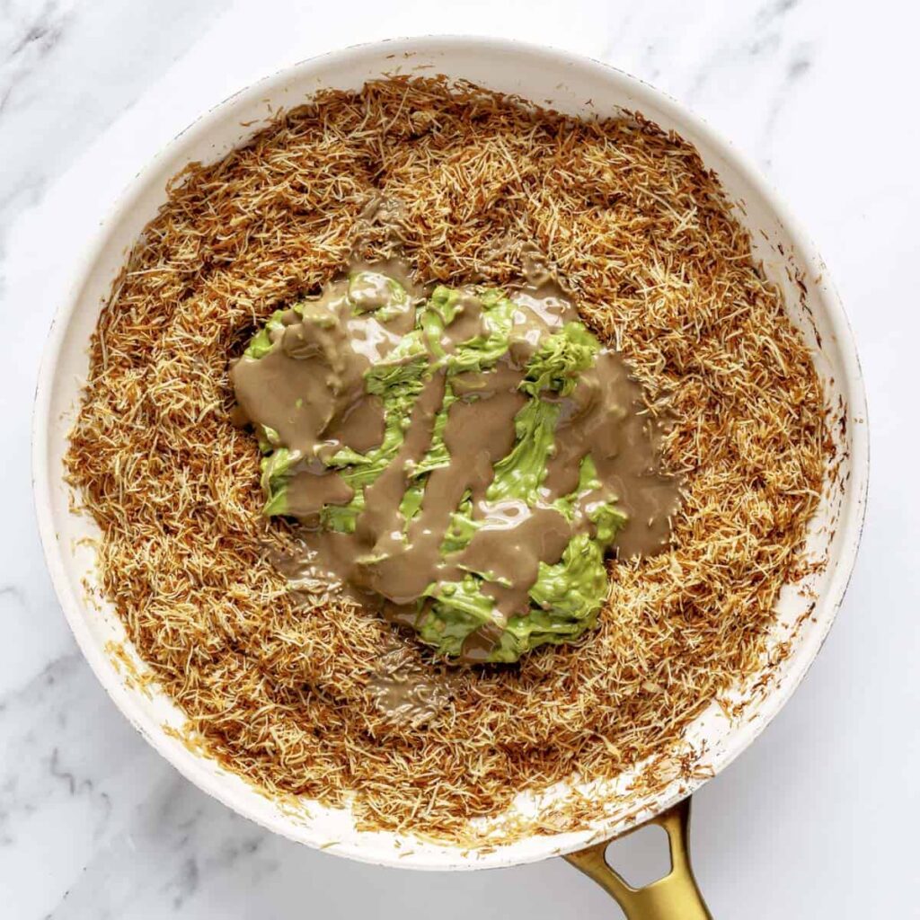 Golden vermicelli with creamy avocado and tahini sauce in a skillet, offering a vibrant, delicious meal option.