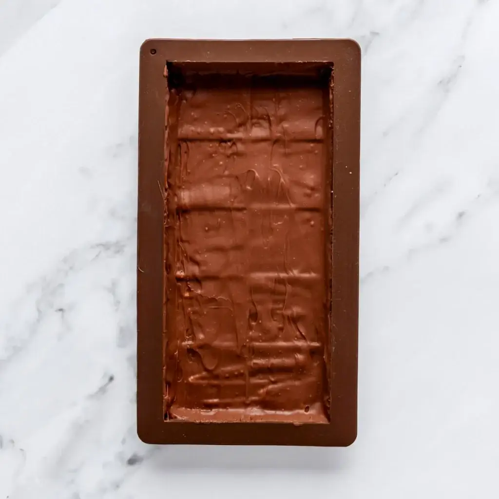 Chocolate slab set in a rectangle mold on a marble surface.