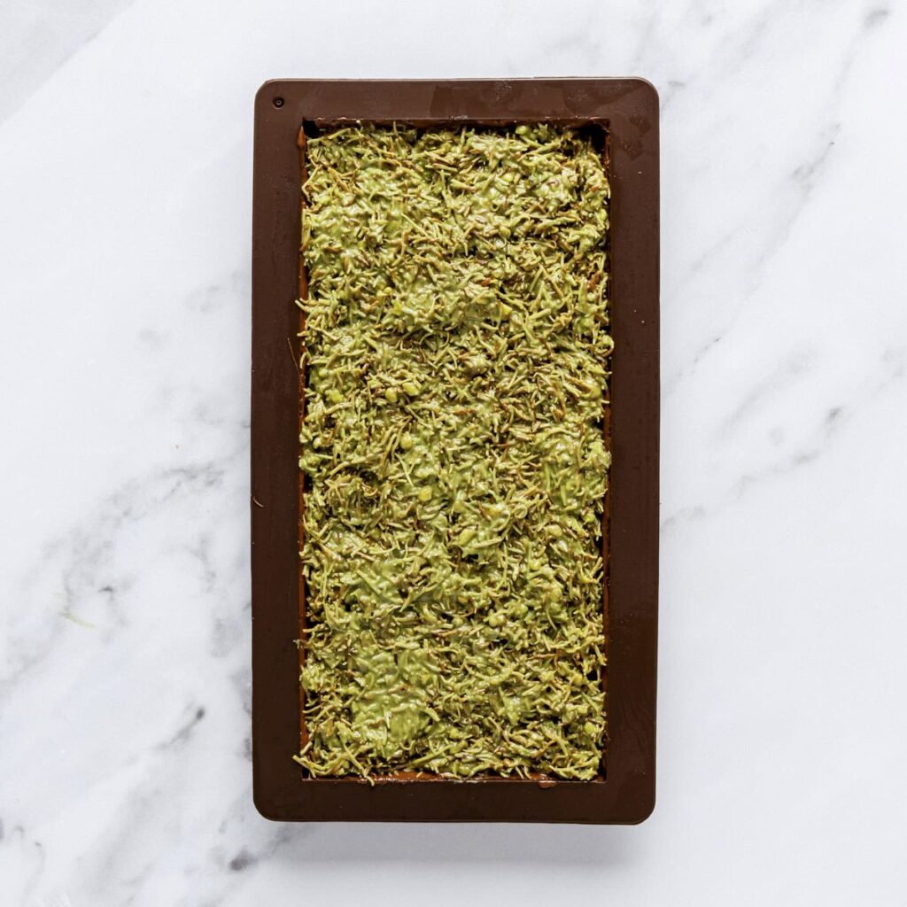 Green pistachio and chocolate bar in a mold on a marble surface.