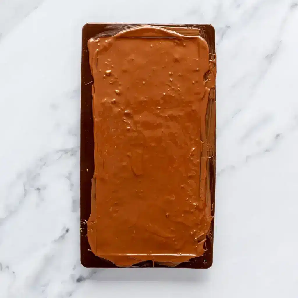 Rich chocolate bar in a mold on a marble surface, ready to set for delicious homemade treats.