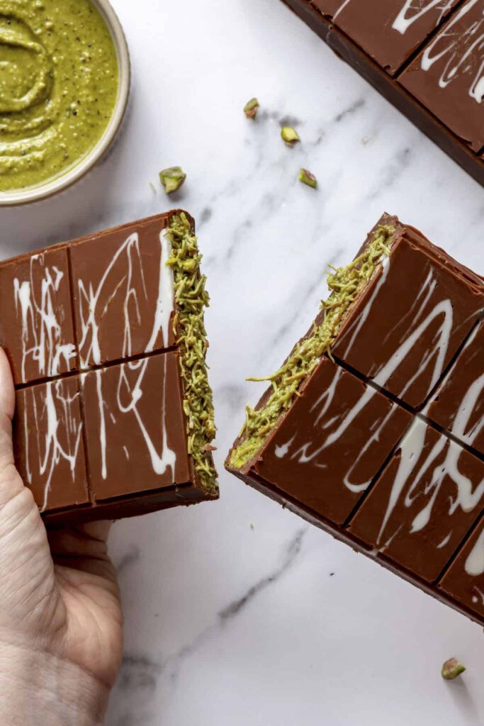 Chocolate pistachio bars with creamy center, marbled top, and pistachio garnish on marble surface.