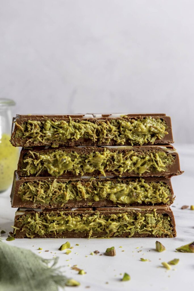 Stack of four pistachio-filled chocolate bars on a white surface, garnished with crushed pistachios.