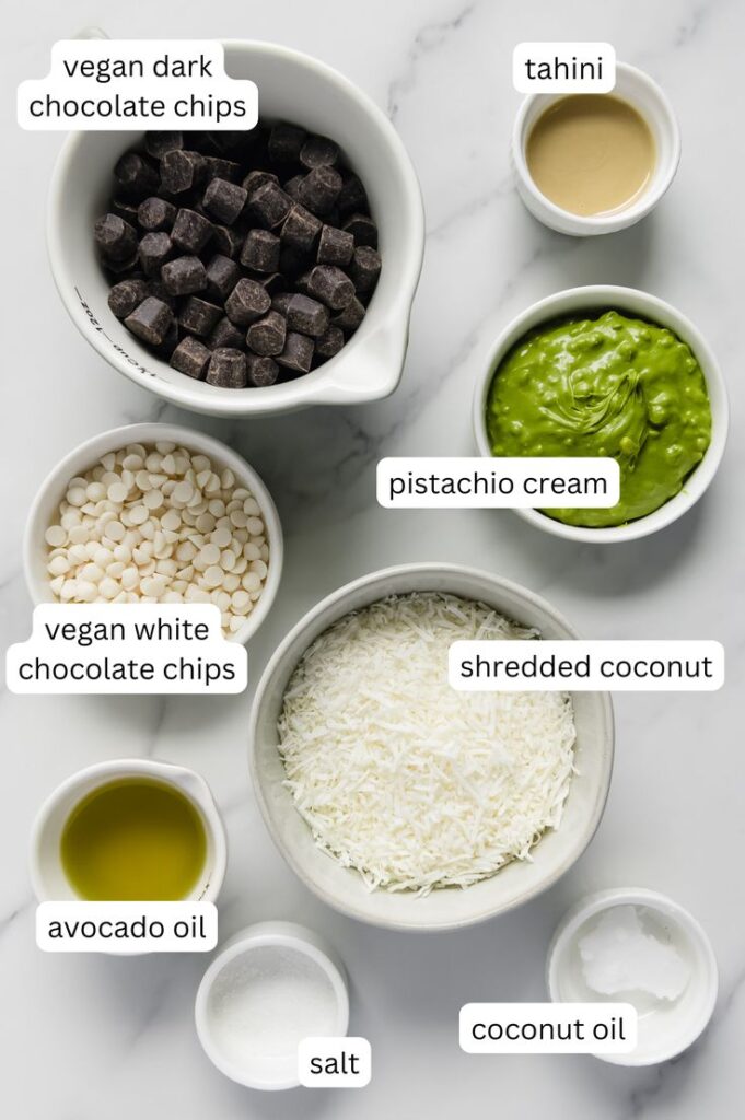 Assorted vegan baking ingredients in bowls: chocolate chips, pistachio cream, shredded coconut, tahini, and oils.