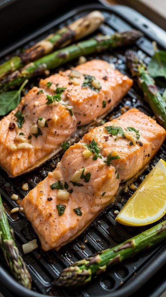 Grilled salmon fillets garnished with herbs and garlic, served with asparagus and a lemon wedge on a pan.