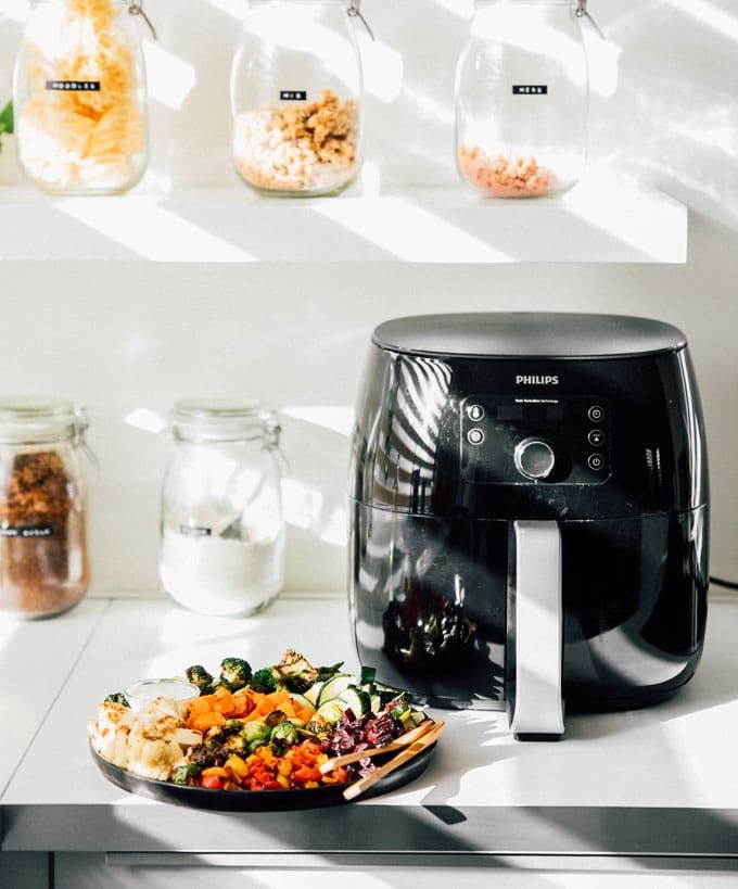 Air fryer on kitchen counter with colorful roasted vegetables; jars of ingredients in the background.
