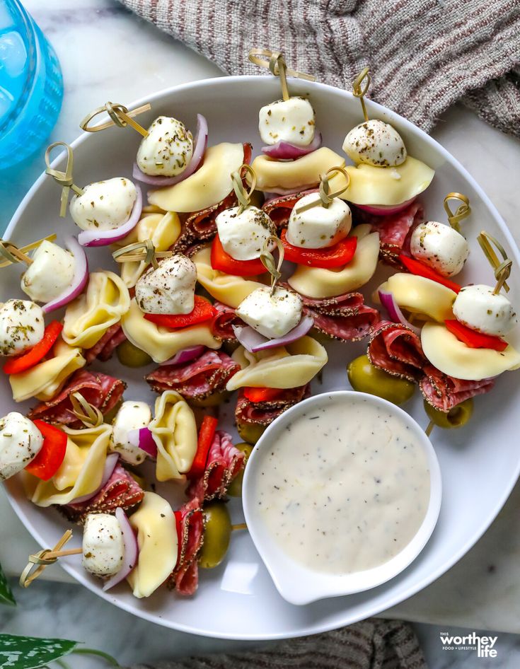 Caprese skewers with mozzarella, salami, tortellini, and peppers on a plate with dip, perfect for party appetizers.