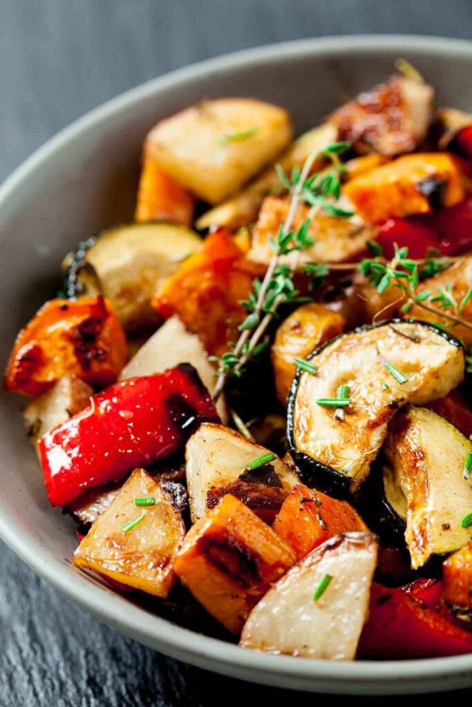 Bowl of colorful roasted vegetables with herbs, featuring zucchini, bell peppers, and sweet potatoes.