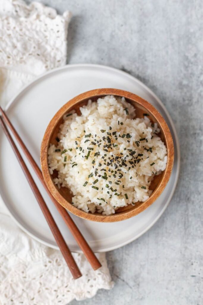 Wooden bowl of seasoned rice with chopsticks on a plate. Perfect side dish or Asian cuisine concept.