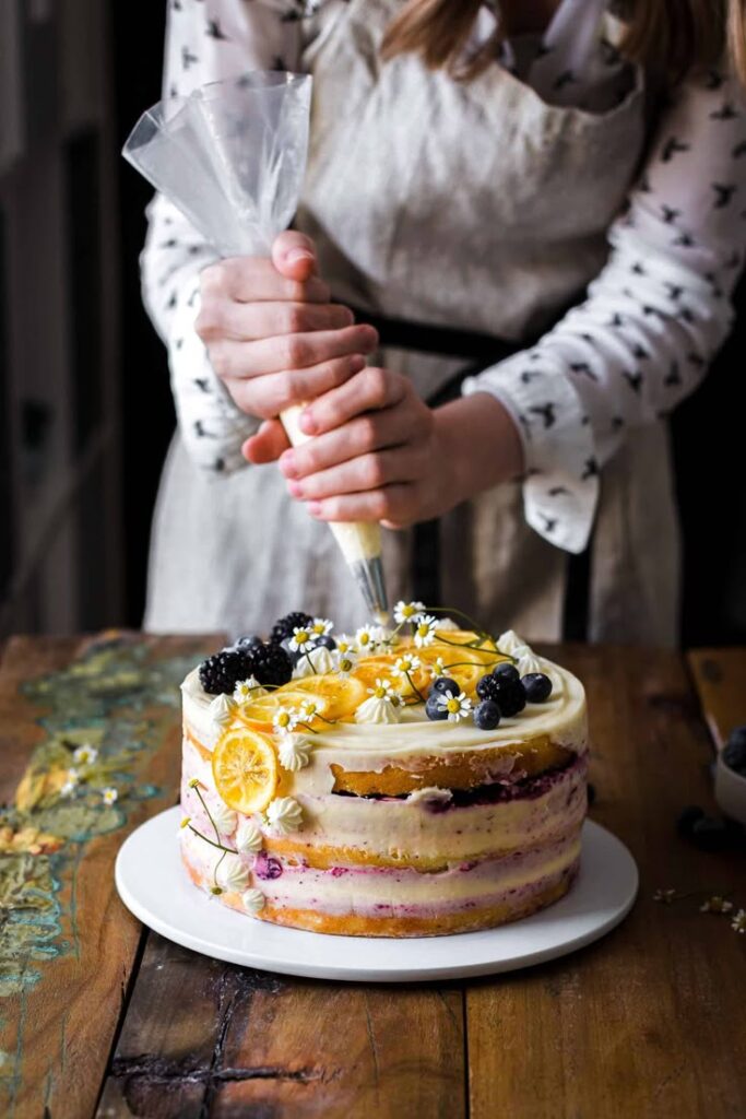 Decorating a layered cake with frosting, lemon slices, and fresh berries on a rustic wooden table.