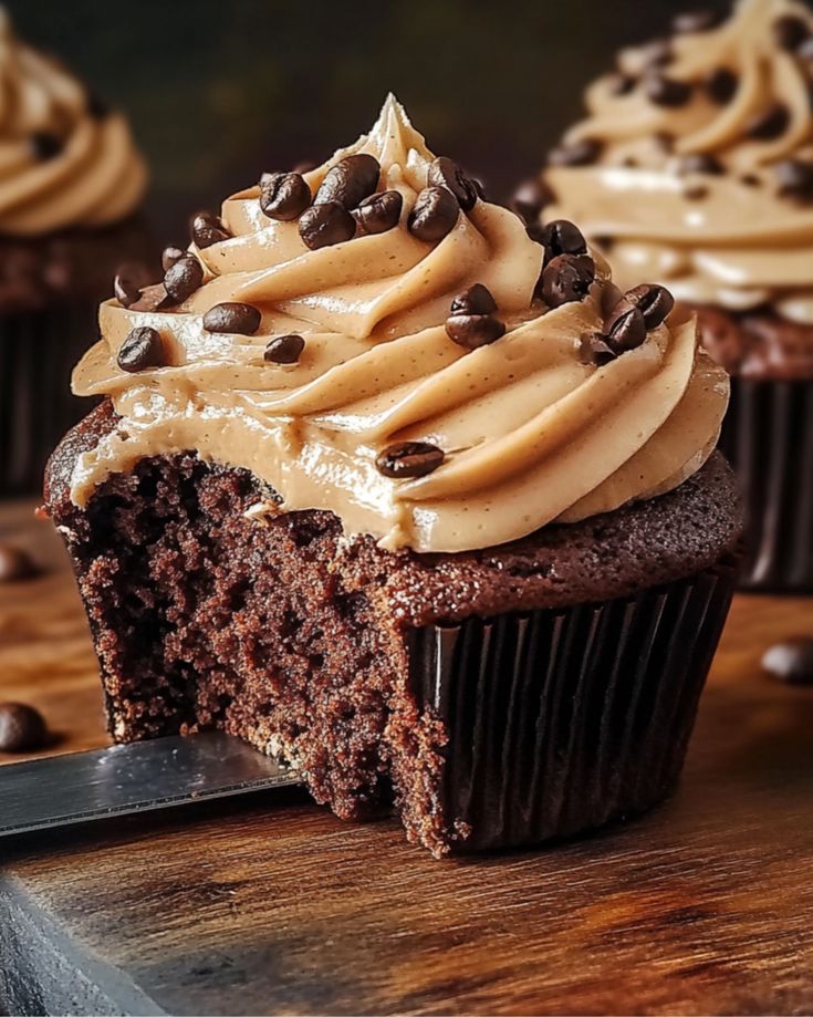 Mocha cupcake with creamy coffee frosting and chocolate chips, placed on a wooden surface, partially eaten.