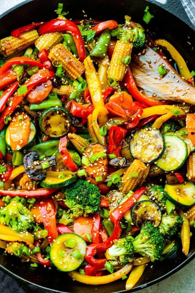 Colorful vegetable stir fry with broccoli, bell peppers, zucchini, carrots, and baby corn in a skillet.