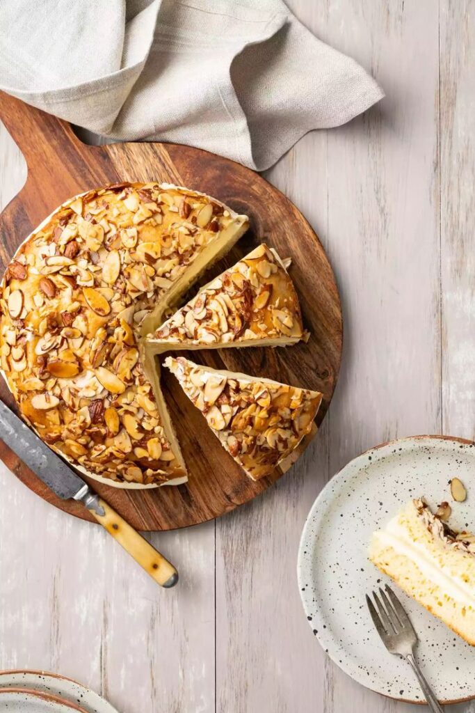 Delicious almond cake on wooden board with a sliced piece on a plate, perfect for dessert lovers.
