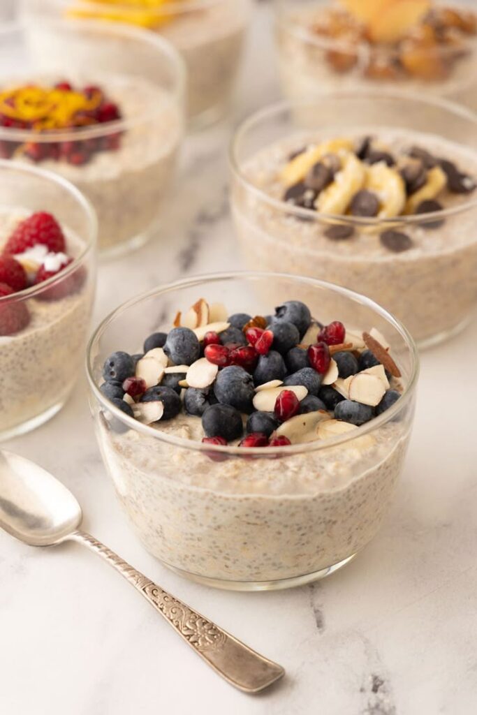Glass bowl of overnight oats topped with blueberries, almonds, and pomegranate seeds on a marble surface.