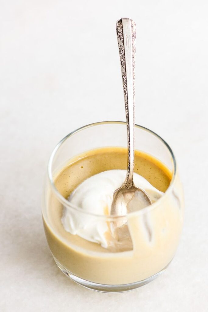 Creamy dessert topped with whipped cream in a glass, with a spoon placed inside.
