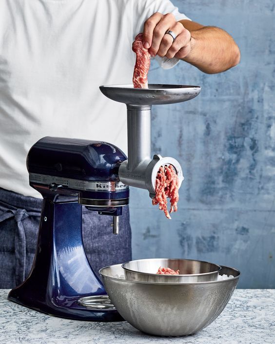 Person grinding meat with a KitchenAid mixer and meat grinder attachment into a metal bowl.