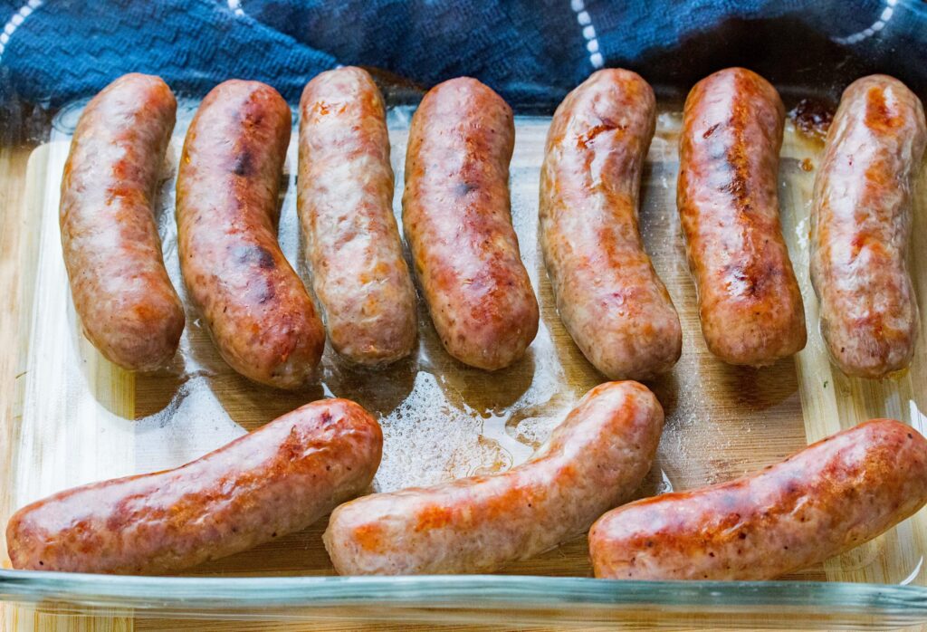 Grilled sausages in glass dish on wooden surface, ready to serve. Delicious and perfectly browned.