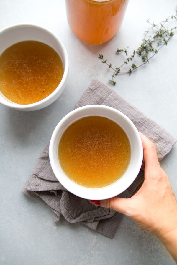 Hand holding a bowl of homemade bone broth, accompanied by thyme sprigs and a linen napkin.
