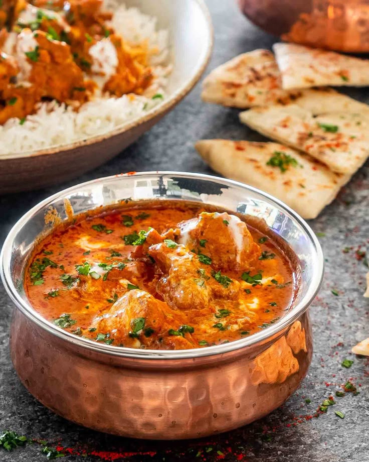 Creamy butter chicken curry in copper bowl, served with naan and rice, garnished with fresh herbs.