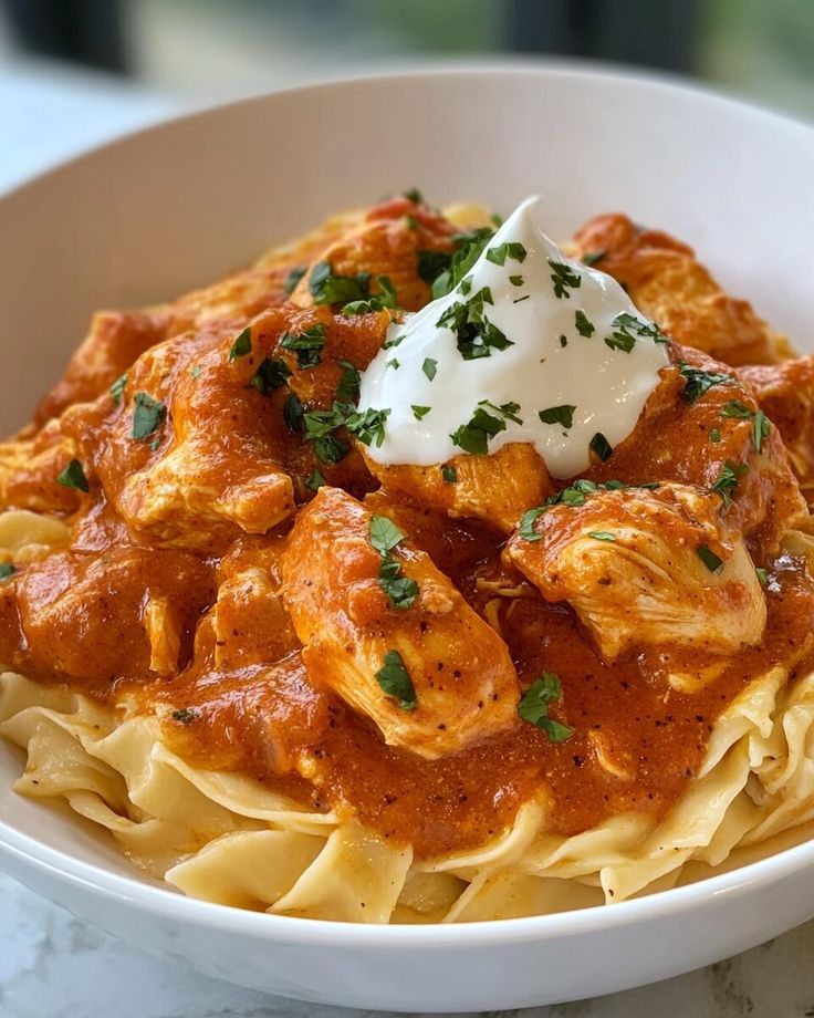Creamy pasta with rich tomato sauce and tender chicken, topped with fresh herbs and a dollop of sour cream.