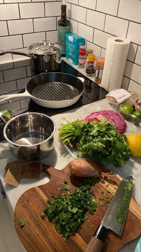 Chopped herbs and ingredients on a kitchen counter with pots and spices, ready for cooking preparation.