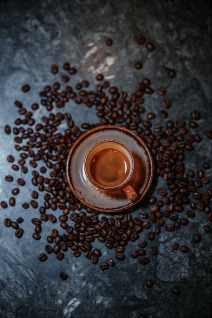 Ceramic cup of coffee surrounded by scattered coffee beans on a dark marble surface.
