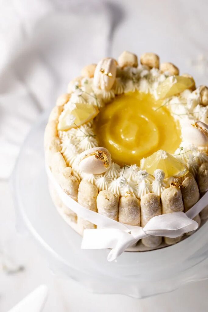 Elegant lemon charlotte cake with creamy frosting, topped with macarons and lemon wedges. Perfect for dessert lovers.