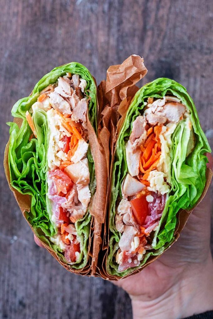 Fresh lettuce wrap filled with grilled chicken, tomatoes, carrots, and cheese on a wooden background.