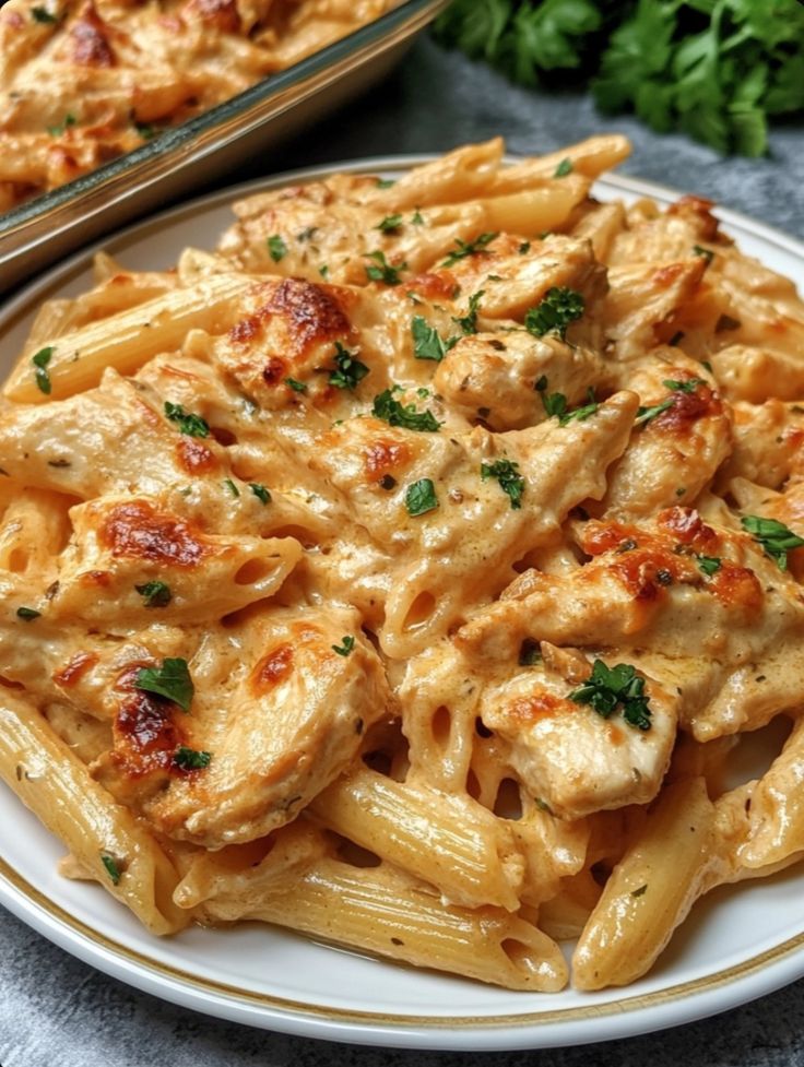 Creamy baked chicken Alfredo pasta garnished with herbs on a white plate, perfect Italian comfort food.