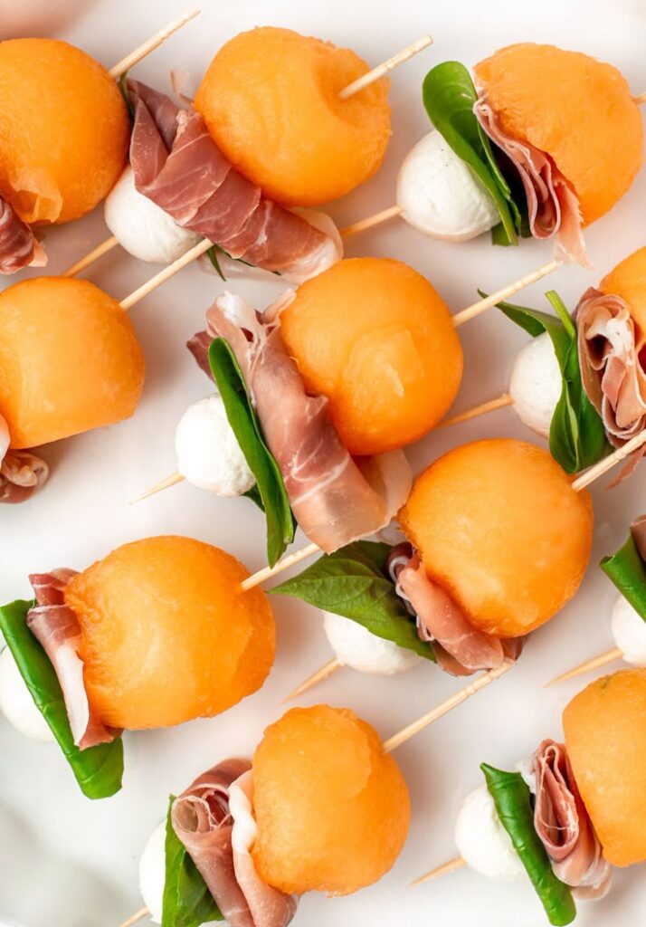 Prosciutto melon skewers with mozzarella and spinach on a platter, perfect for a fresh and tasty appetizer.