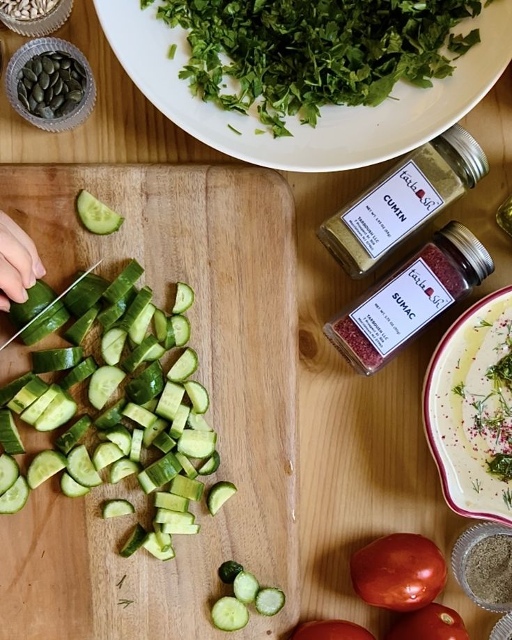 Preparing a fresh salad with chopped cucumbers, herbs, spices, and tomatoes on a wooden cutting board.
