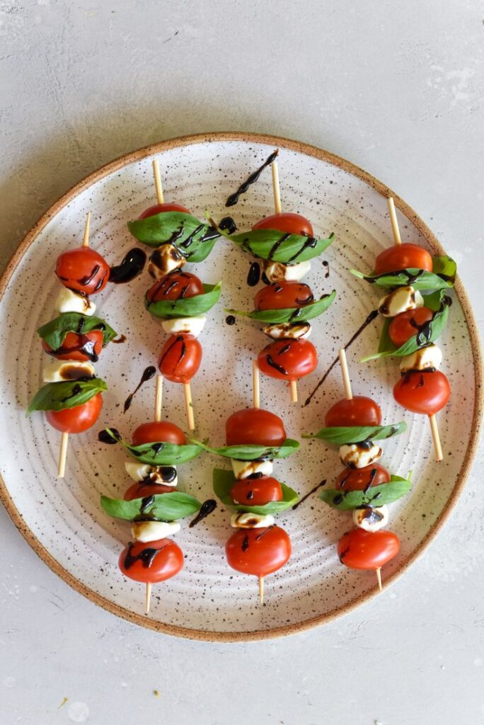 Caprese skewers with cherry tomatoes, mozzarella, basil, and balsamic glaze on a plate. Perfect appetizer.