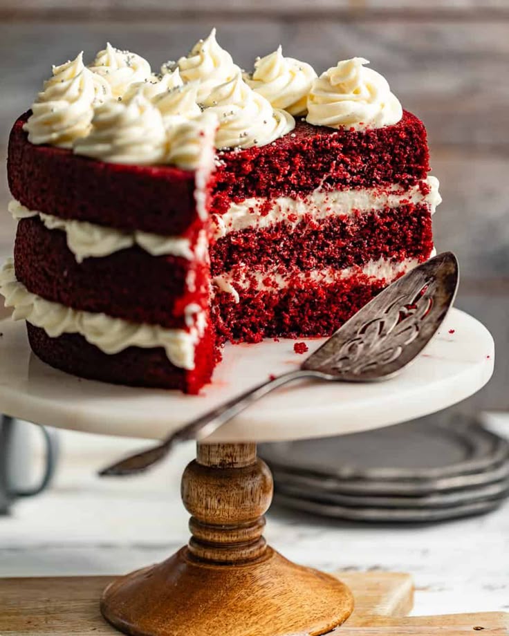 Decadent red velvet cake with cream cheese frosting on a wooden stand, slice removed.