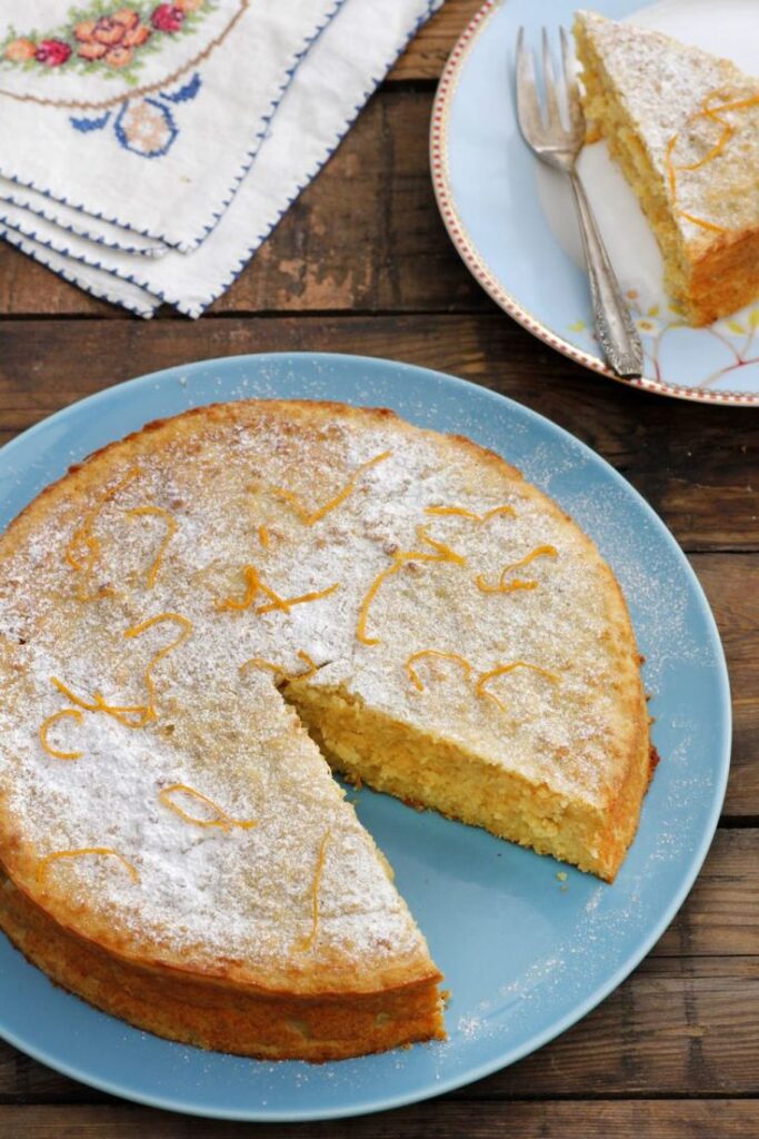 Lemon cake with powdered sugar on a blue plate, one slice served on a dish for a delightful dessert moment.