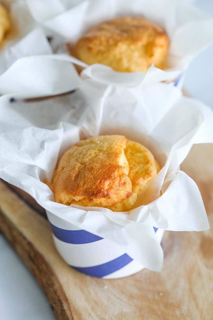Golden muffins in striped paper cups on a wooden board, wrapped in white baking paper.