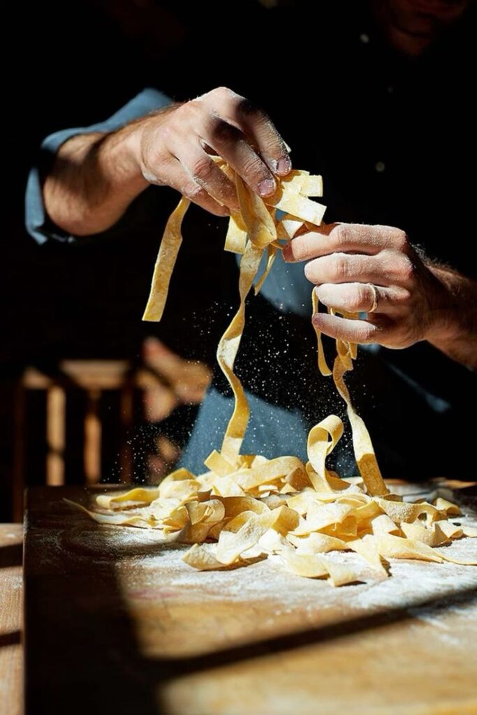Hands making fresh pasta from scratch on a floured wooden table, capturing the art of homemade Italian cuisine.