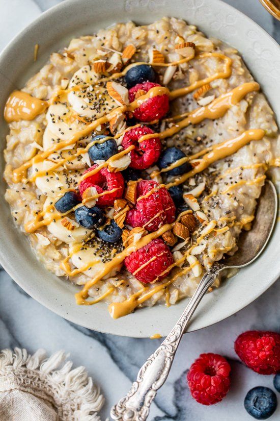 Bowl of oatmeal topped with bananas, berries, almonds, and chia seeds, drizzled with peanut butter.