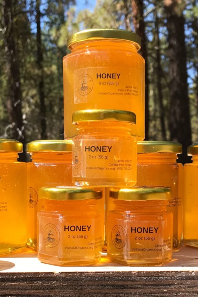 Stacked jars of organic honey with golden lids, set outdoors against a forest background.