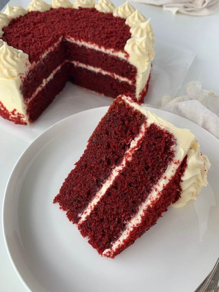 Slice of rich red velvet cake with cream cheese frosting on a white plate.