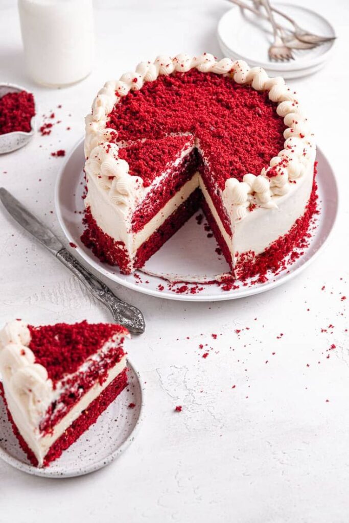 Elegant red velvet cake with cream cheese frosting on a plate, with a slice on the side. Perfect dessert for celebrations.